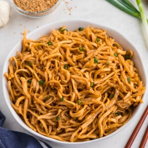 Spicy noodles tossed with sauce, served in a white bowl with chopsticks next to the bowl.