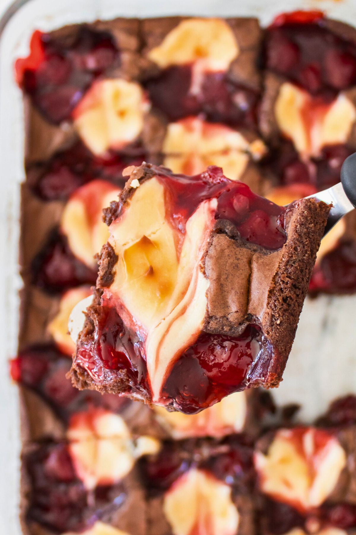 Strawberry swirled cheesecake brownies after being baked, sliced, and once slice lifted on a spatula. 