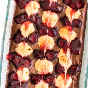 Baked strawberry cheesecake swirled together on top of brownies in a glass dish.