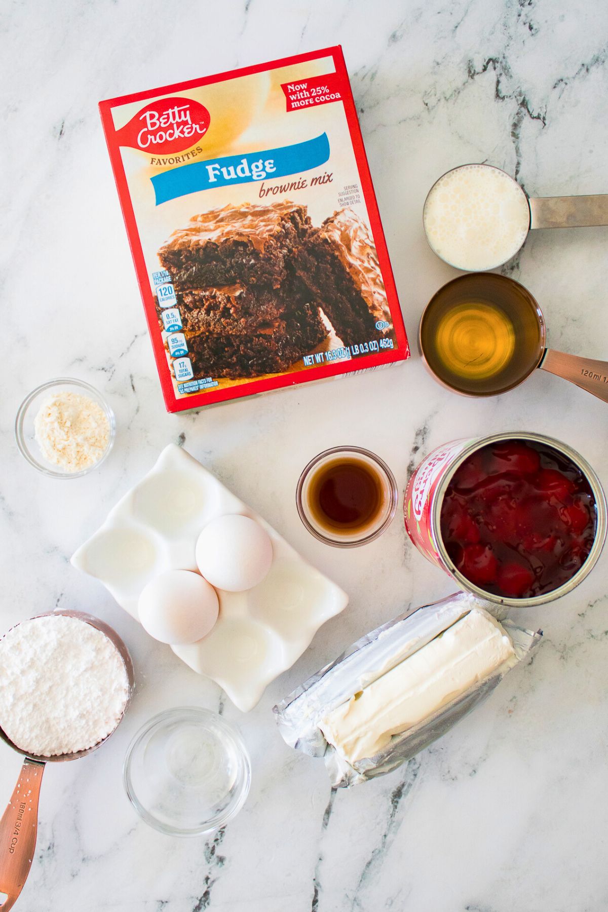 Ingredients for strawberry cheesecake brownies measured out on a marble table. 