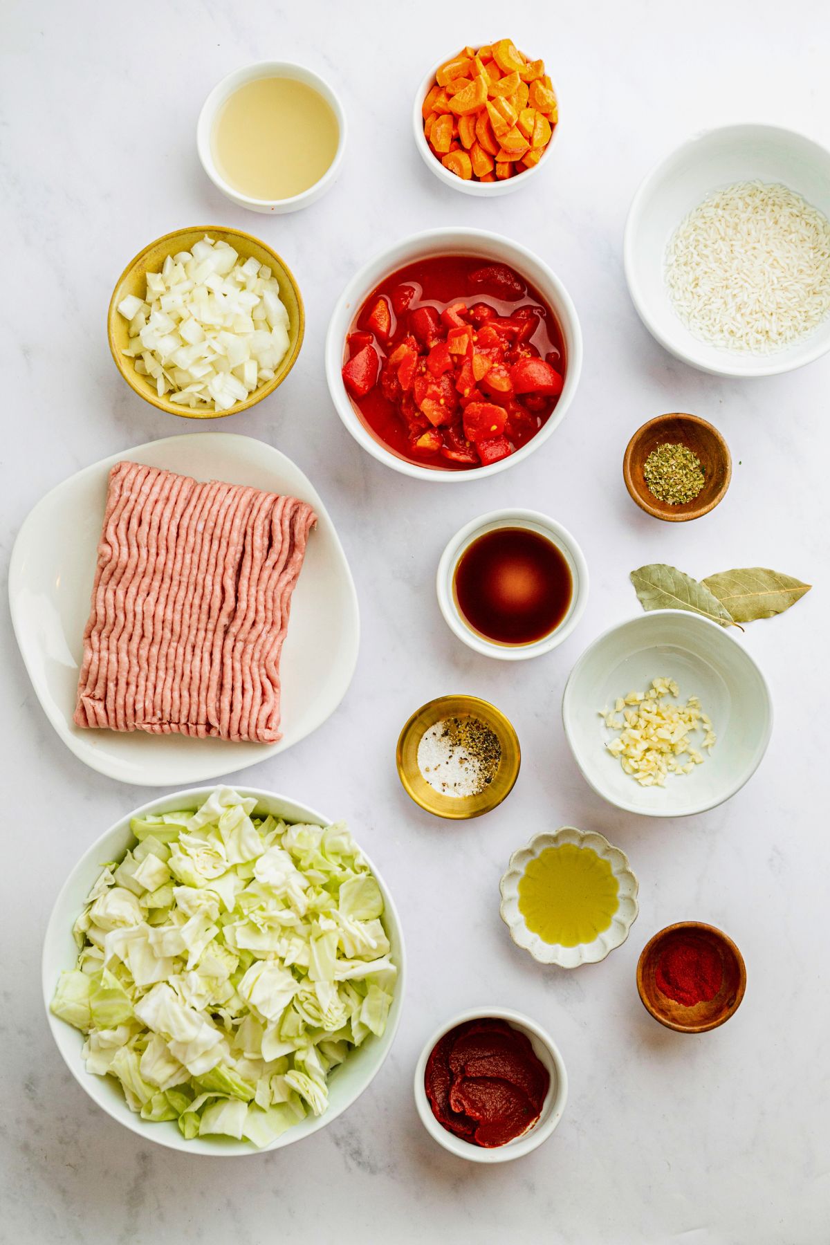 Ingredients needed to make cabbage roll soup measured onto a white marble table. 