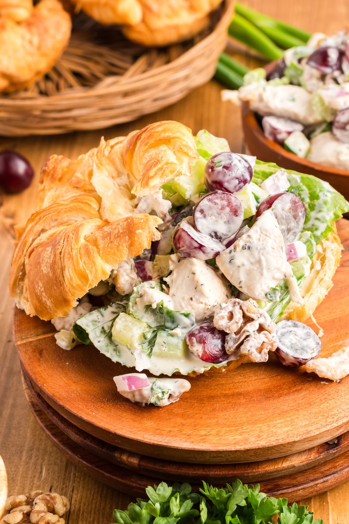 Creamy chicken salad with nuts and grapes, in a croissant on a wooden plate. 