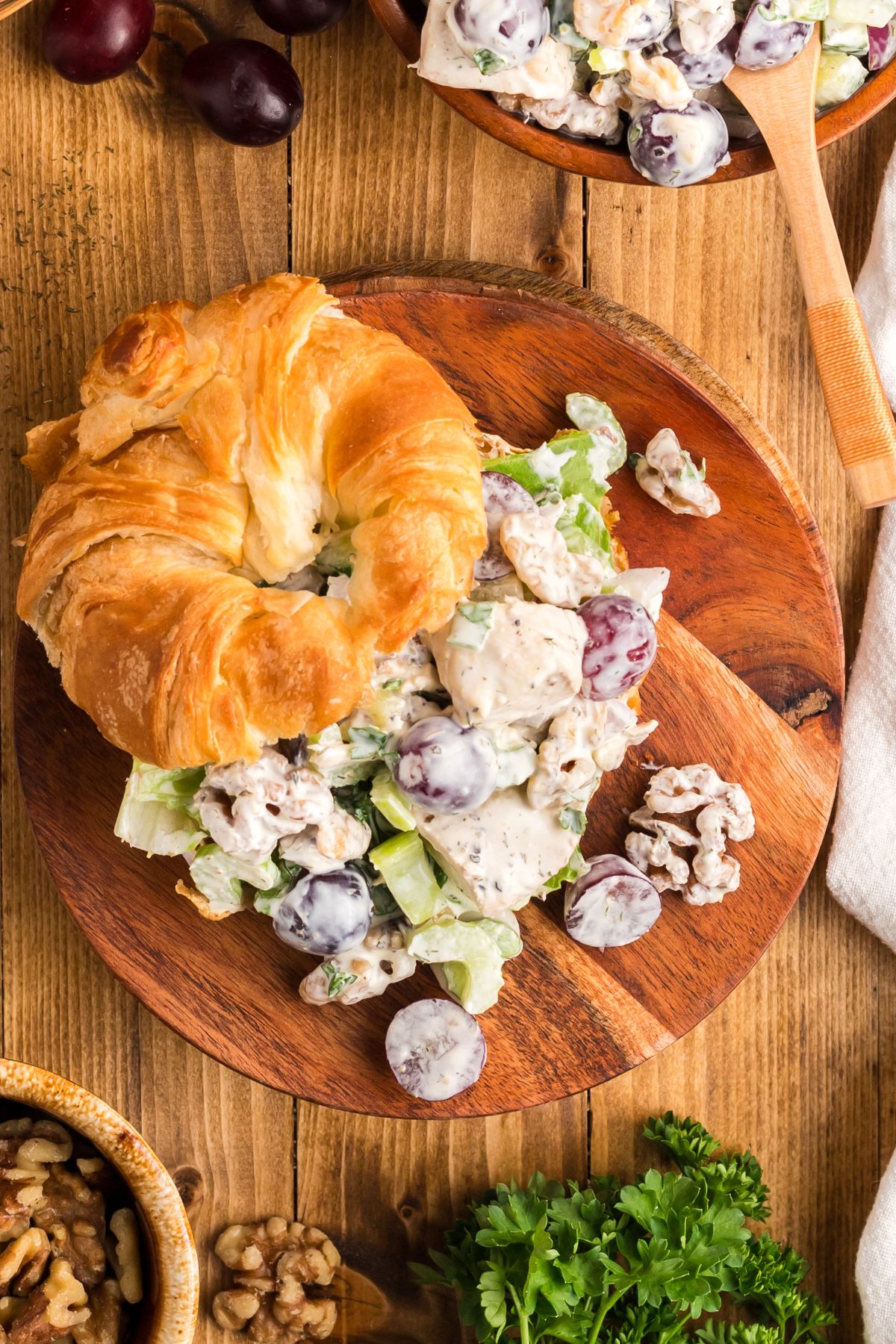 Overhead image of a sandwich made with croissant bread, on a wooden plate. 