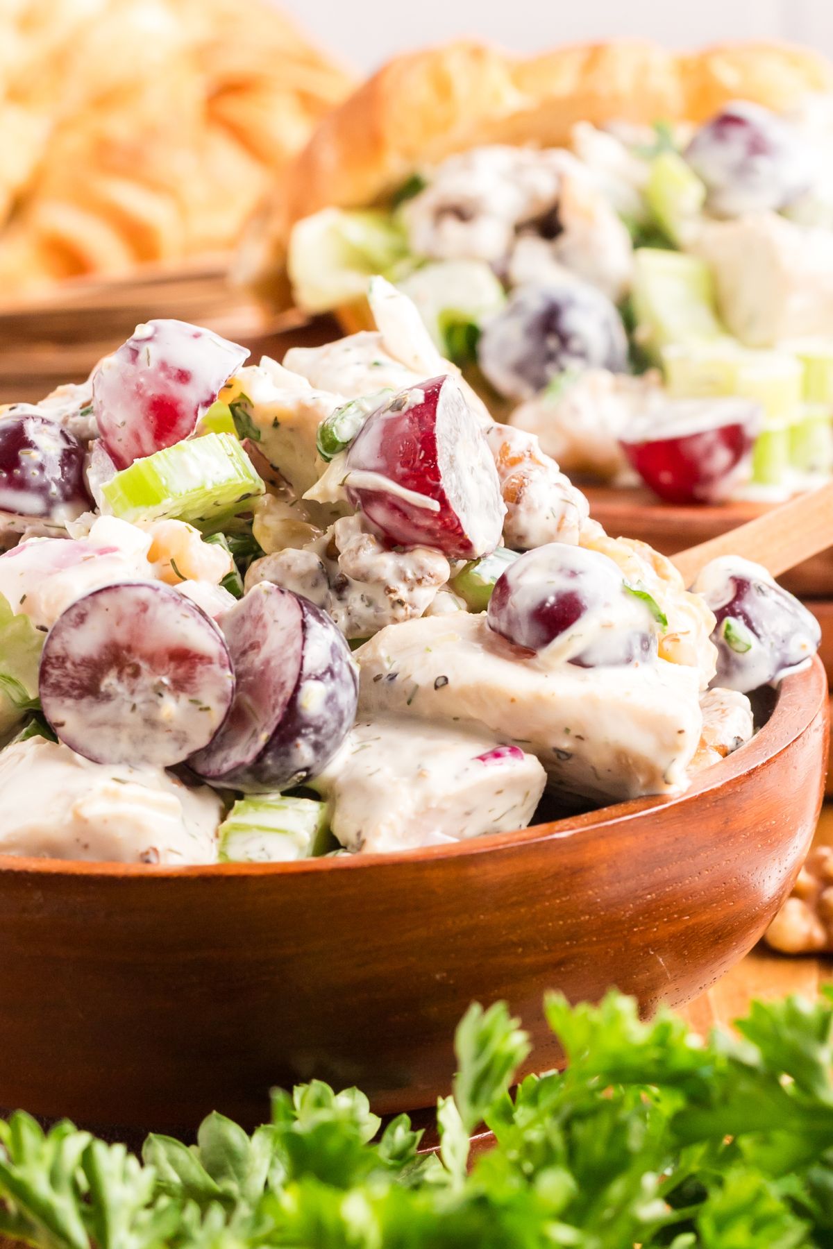 Creamy and colorful chicken salad in a wooden bowl with greens in front of the bow. 