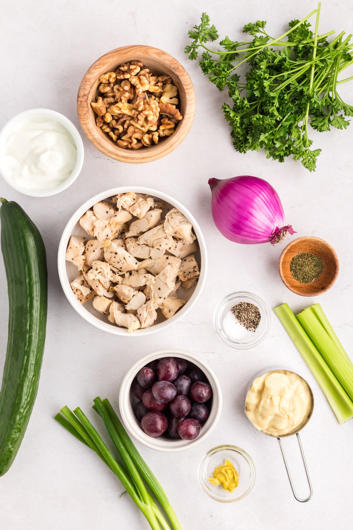 Ingredients needed to make chicken salad, measured into small bowls on a marble table. 