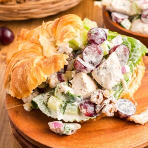 Creamy chicken salad with nuts and grapes, in a croissant on a wooden plate.