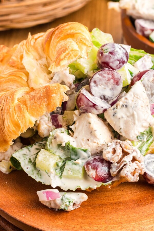 Creamy chicken salad with nuts and grapes, in a croissant on a wooden plate.