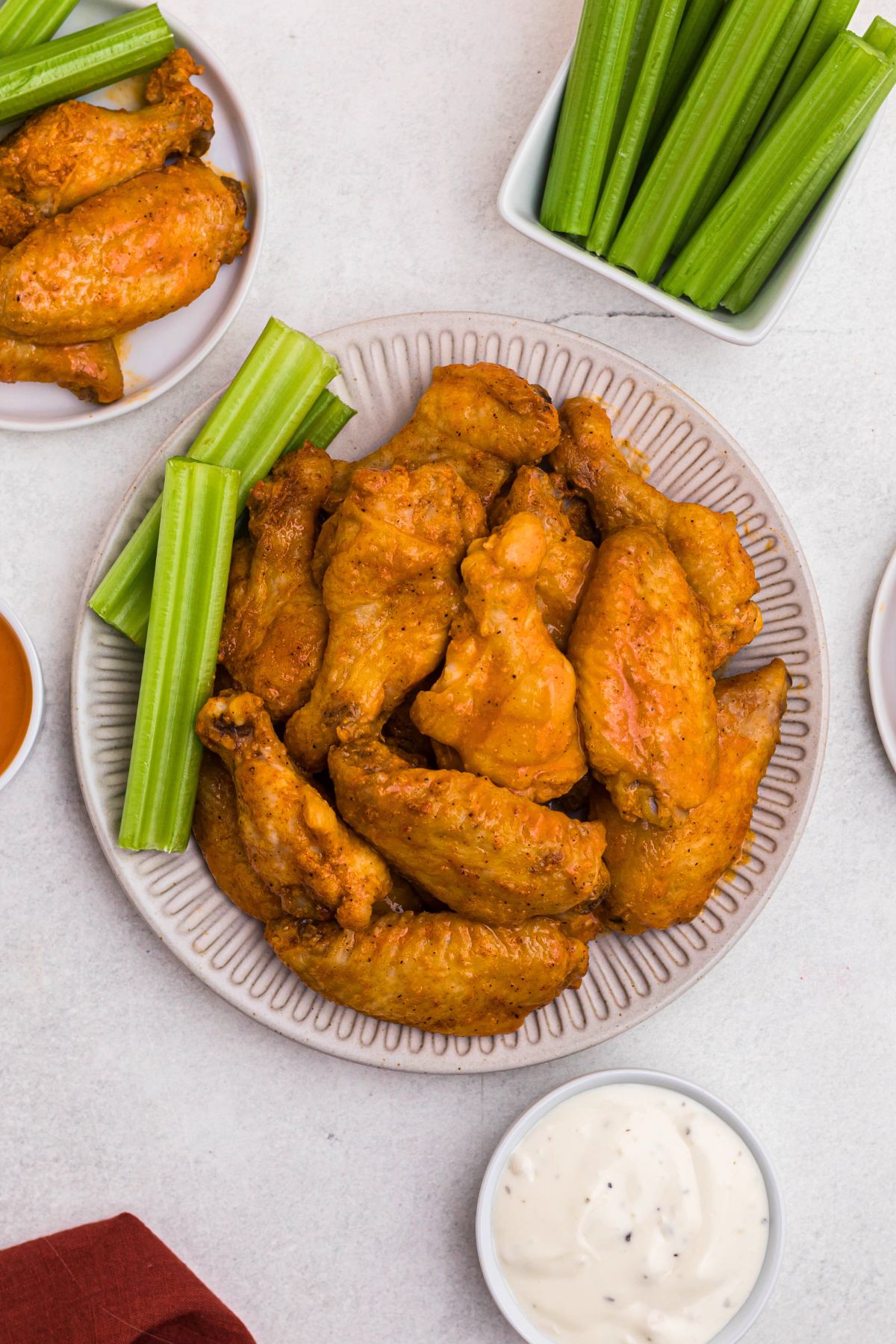 Chicken wings tossed in buffalo sauce on a white plate with celery sauce. 