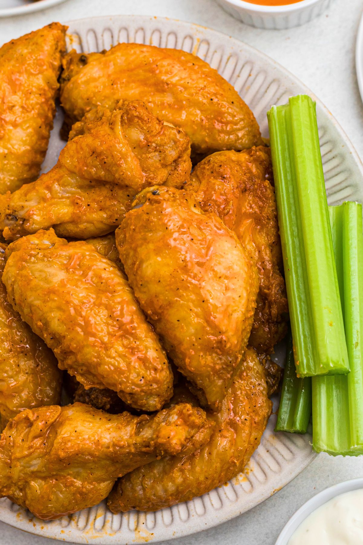 Chicken wings tossed in buffalo sauce on a white plate with celery sauce.