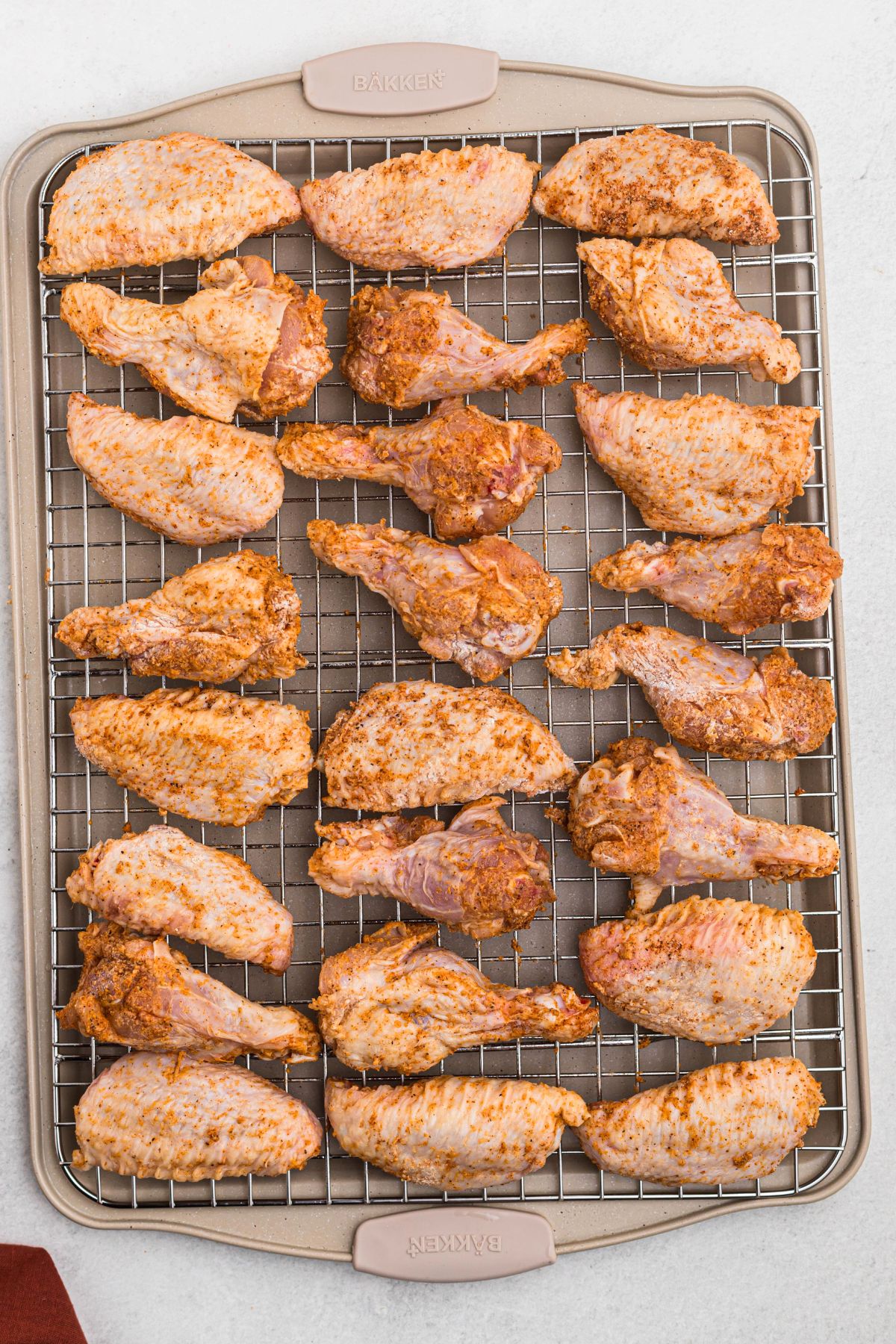 Uncooked chicken wings, tossed in seasonings and placed on a rack over a baking sheet. 