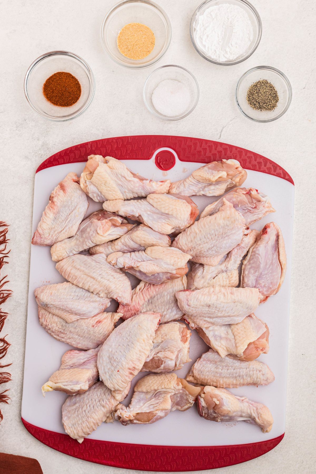 Uncooked chicken wings on a cutting board with seasonings measured in small glass bowls. 