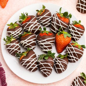 hocolate covered strawberries on a white plate sitting on a pink table.