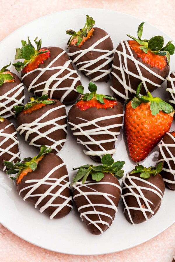 hocolate covered strawberries on a white plate sitting on a pink table.