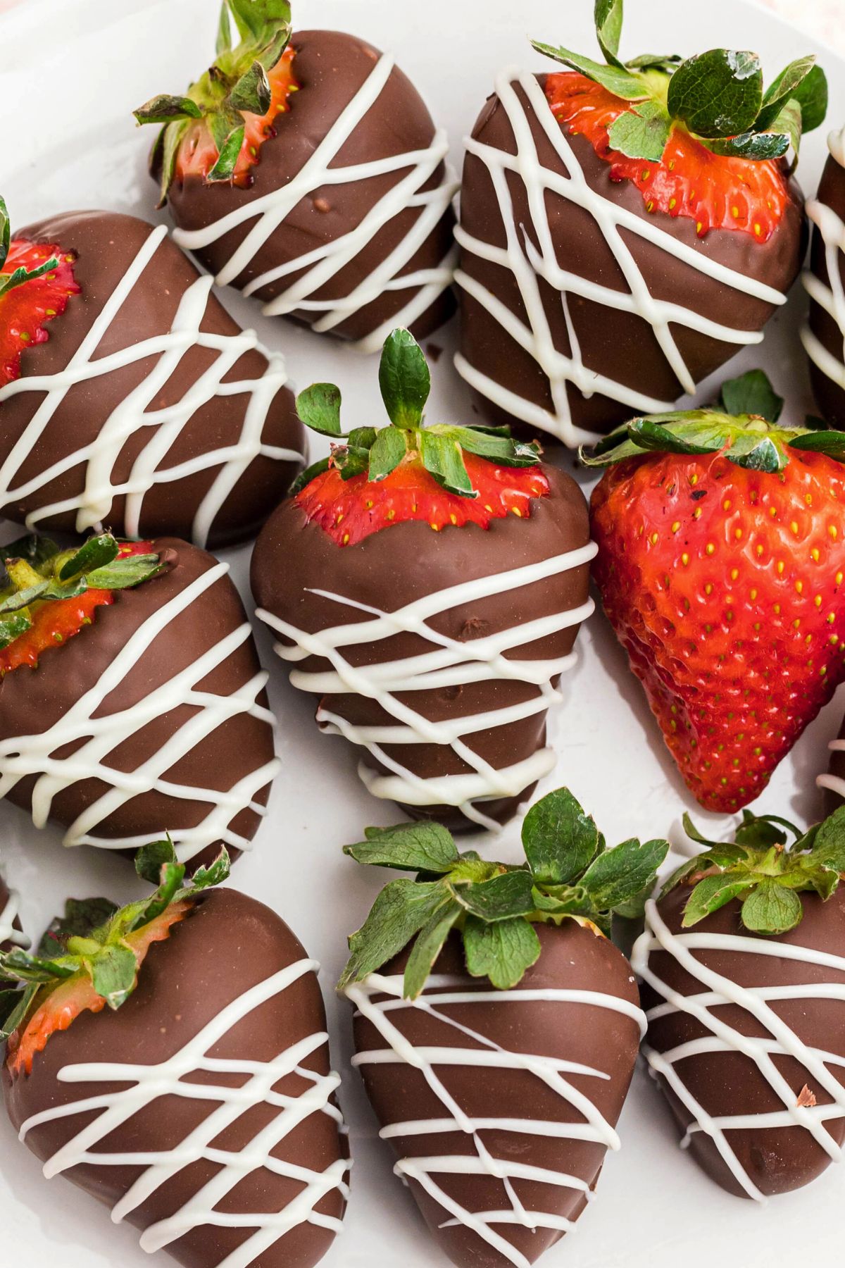 Strawberries coated with chocolate and white chocolate stripes, on a white plate with fresh strawberry in the center of plate. 