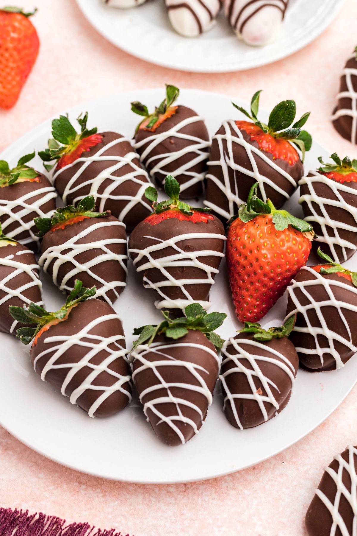 Chocolate strawberries on a white plate sitting on a pink table.