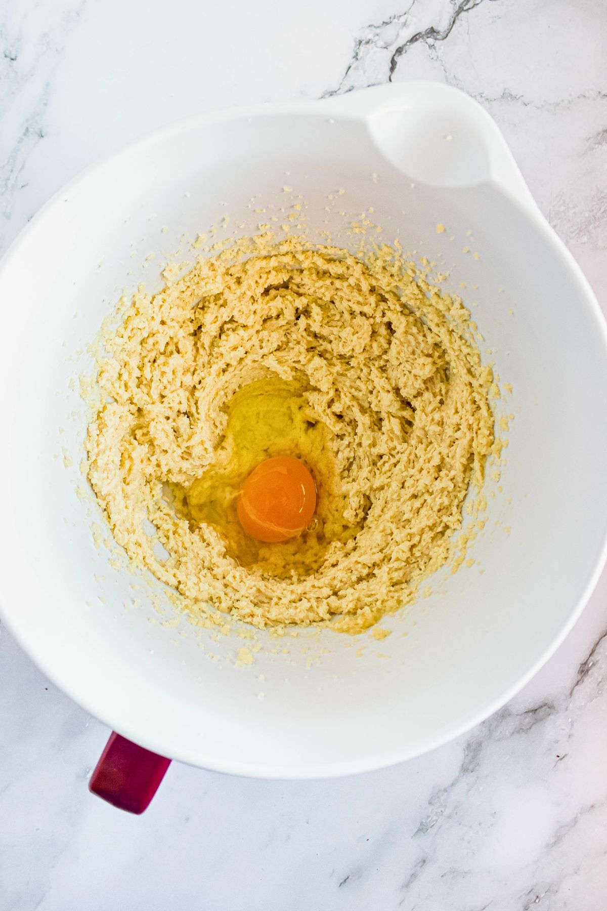 egg being mixed into cake batter in a white bowl. 