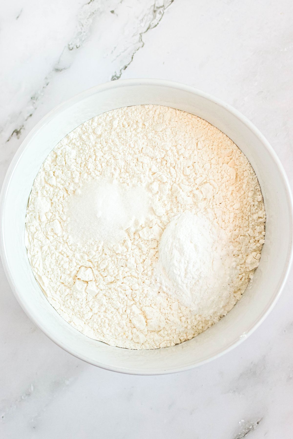 Flour and other dry ingredients being mixed together in a white bowl. 