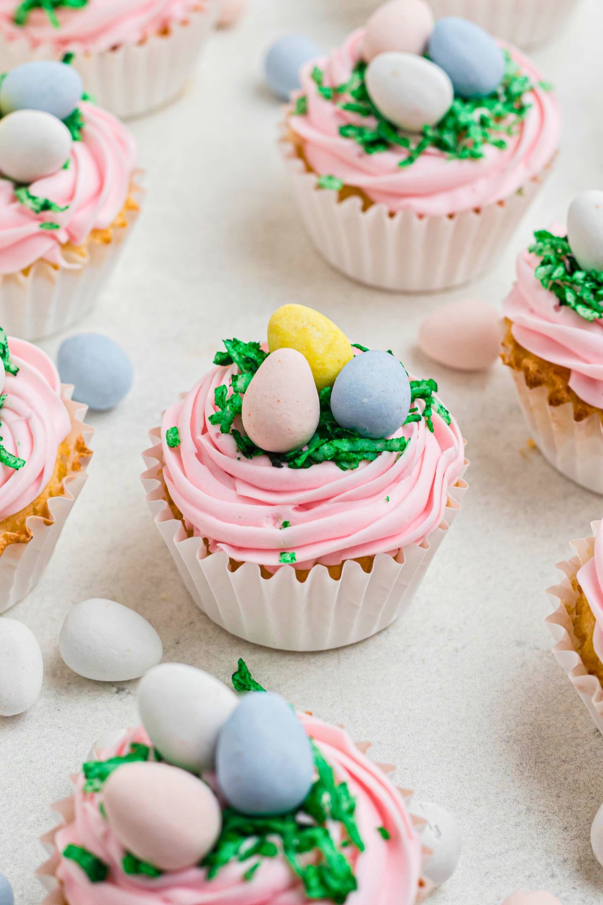 Vanilla cupcakes topped with pink frosting, green coconut, and egg shaped chocolates.