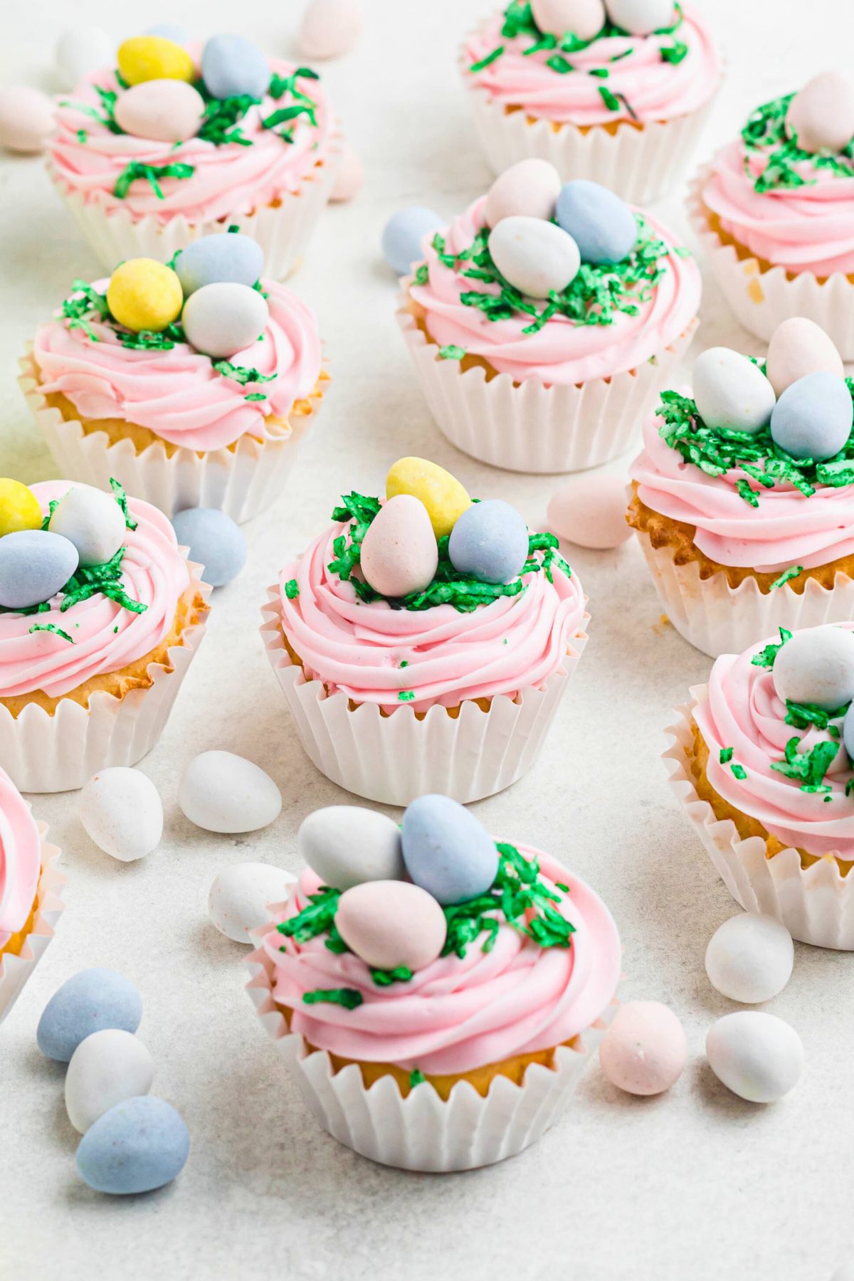 Vanilla cupcakes topped with pink frosting, green coconut, and egg shaped chocolates. 