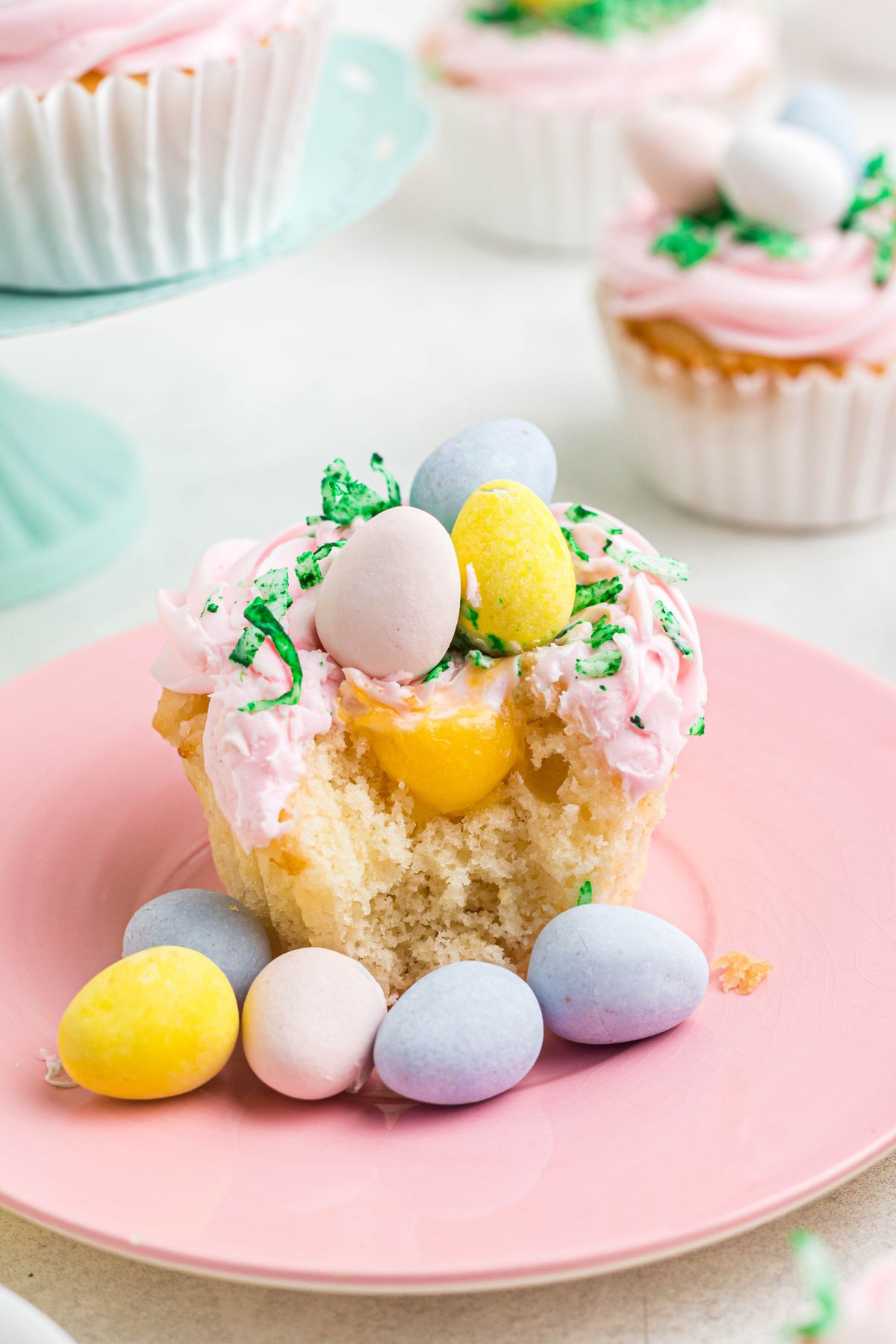 Lemon curd filled cupcake on a pink plate, with chocolate eggs on the plate in front. 