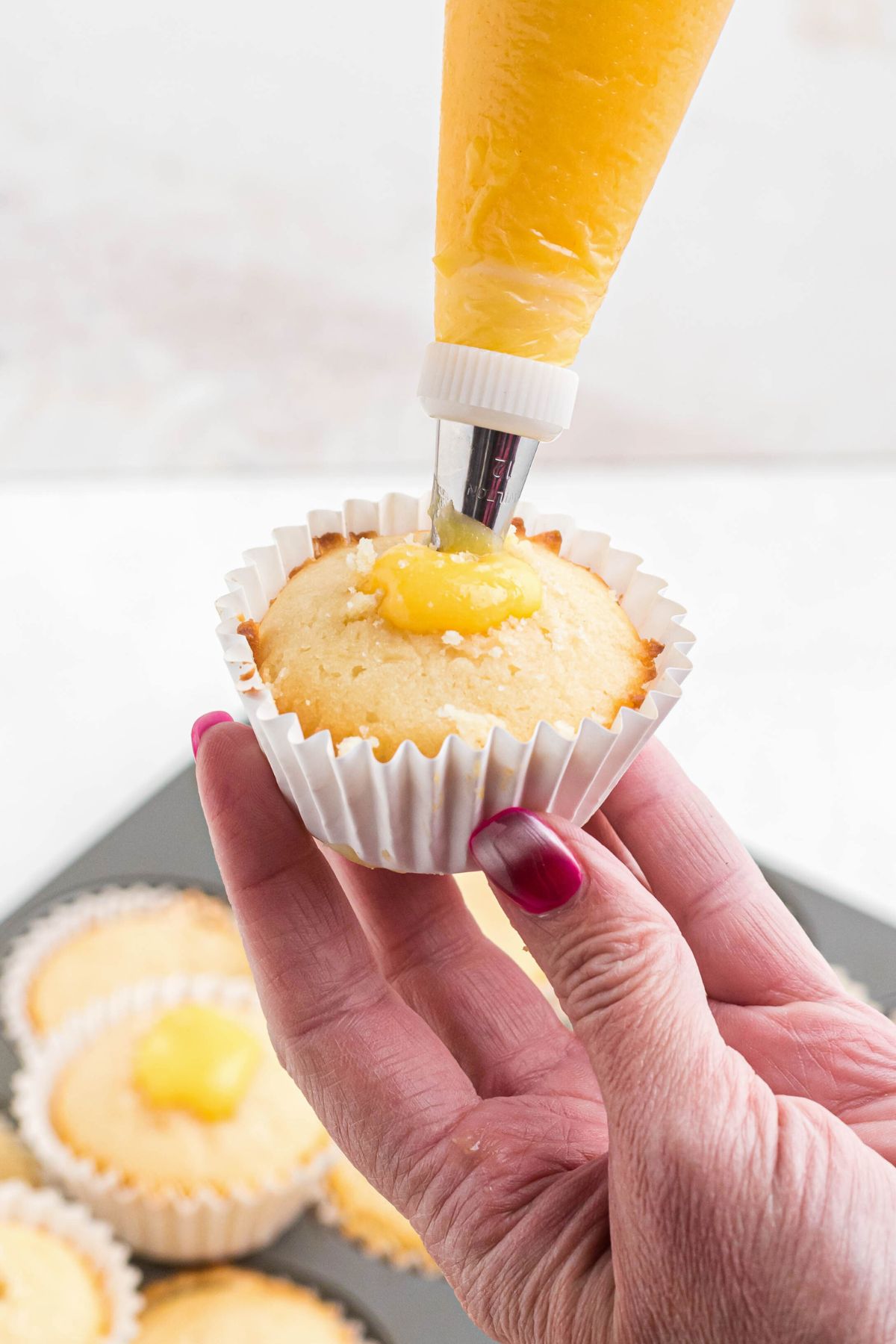 Lemon curd being piped into the center of a vanilla cupcake. 