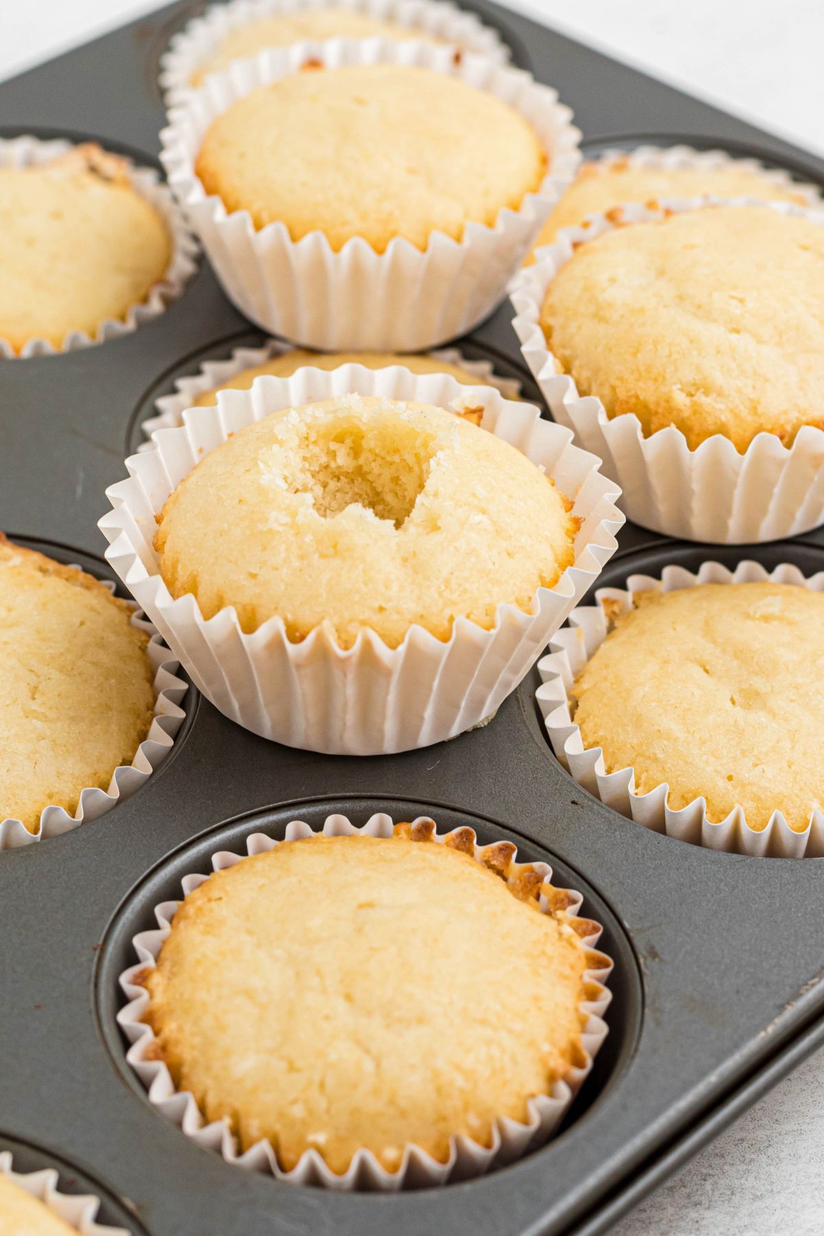 Freshly baked cupcakes, with a scoop being removed from the center of the cupcake. 