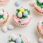 Vanilla cupcakes topped with pink frosting, green coconut, and egg shaped chocolates.