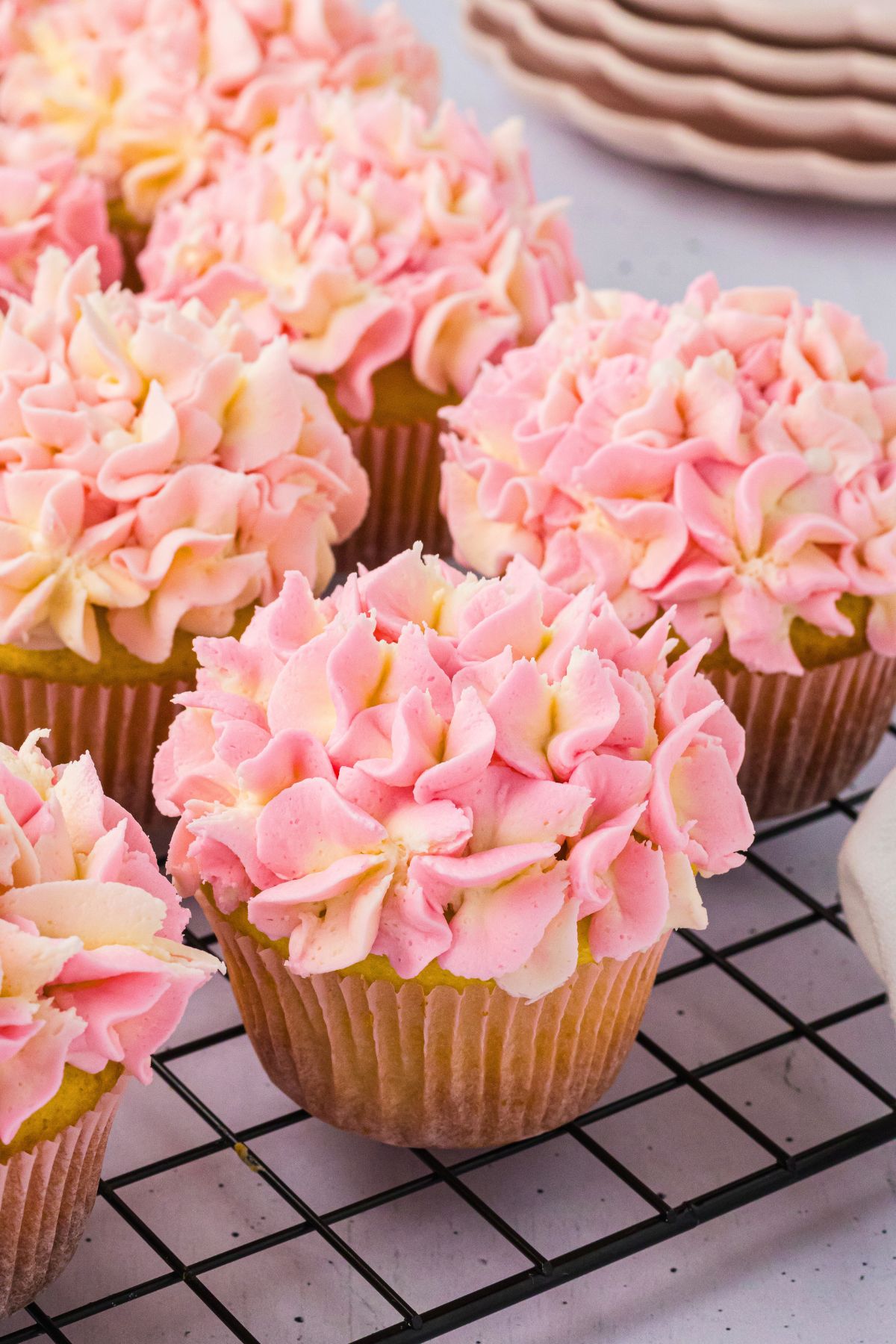 Pink and white hydrangea frosted cupcakes on a metal cooling wrack. 