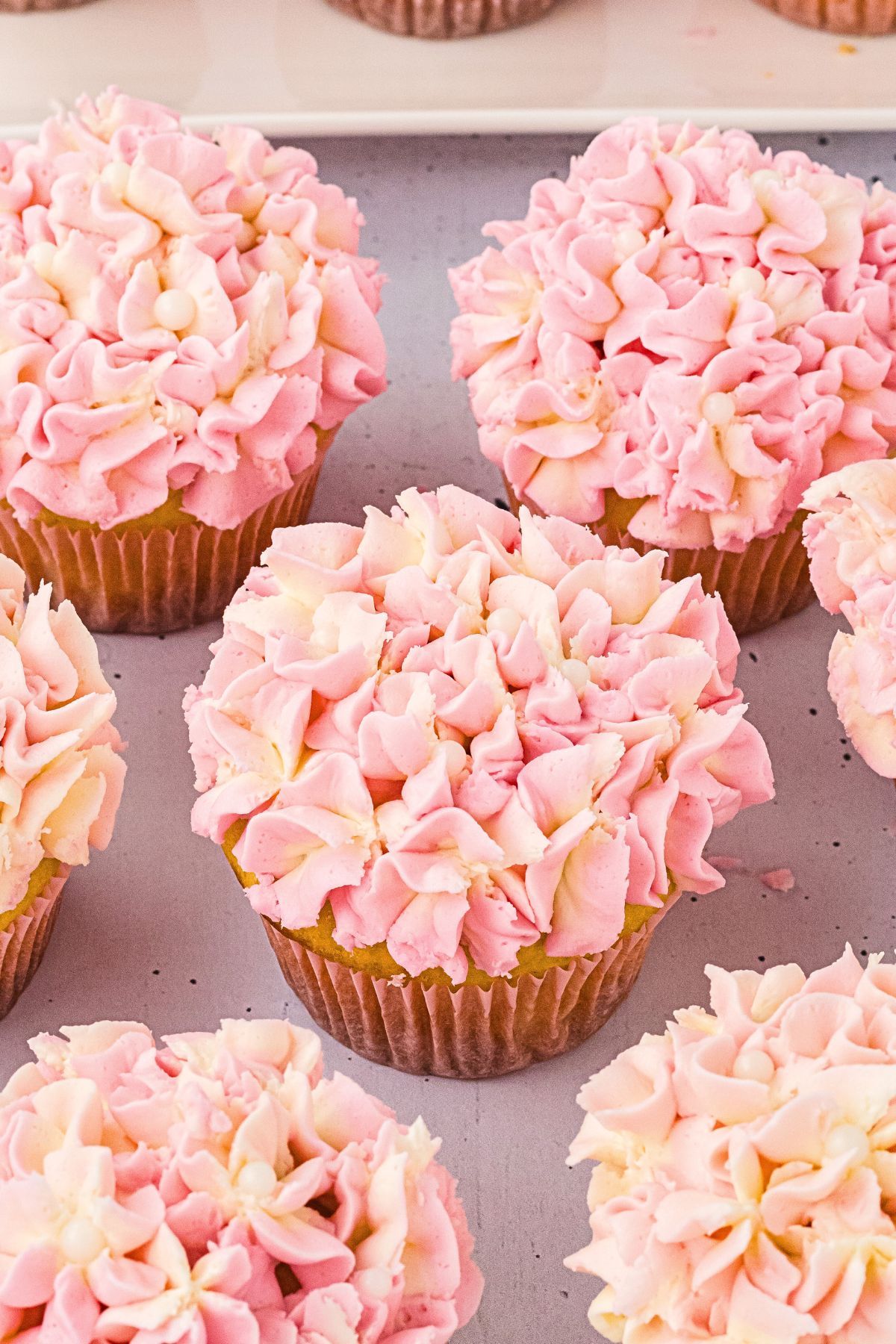 Frosted pink hydrangea cupcakes on a white table. 