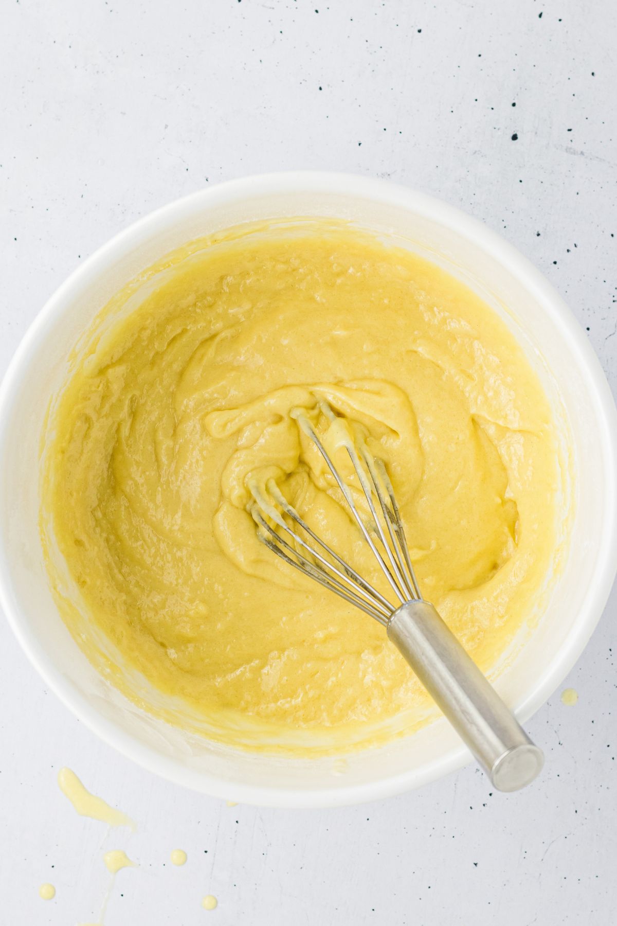 Cake batter being whisked together in a white mixing bowl. 