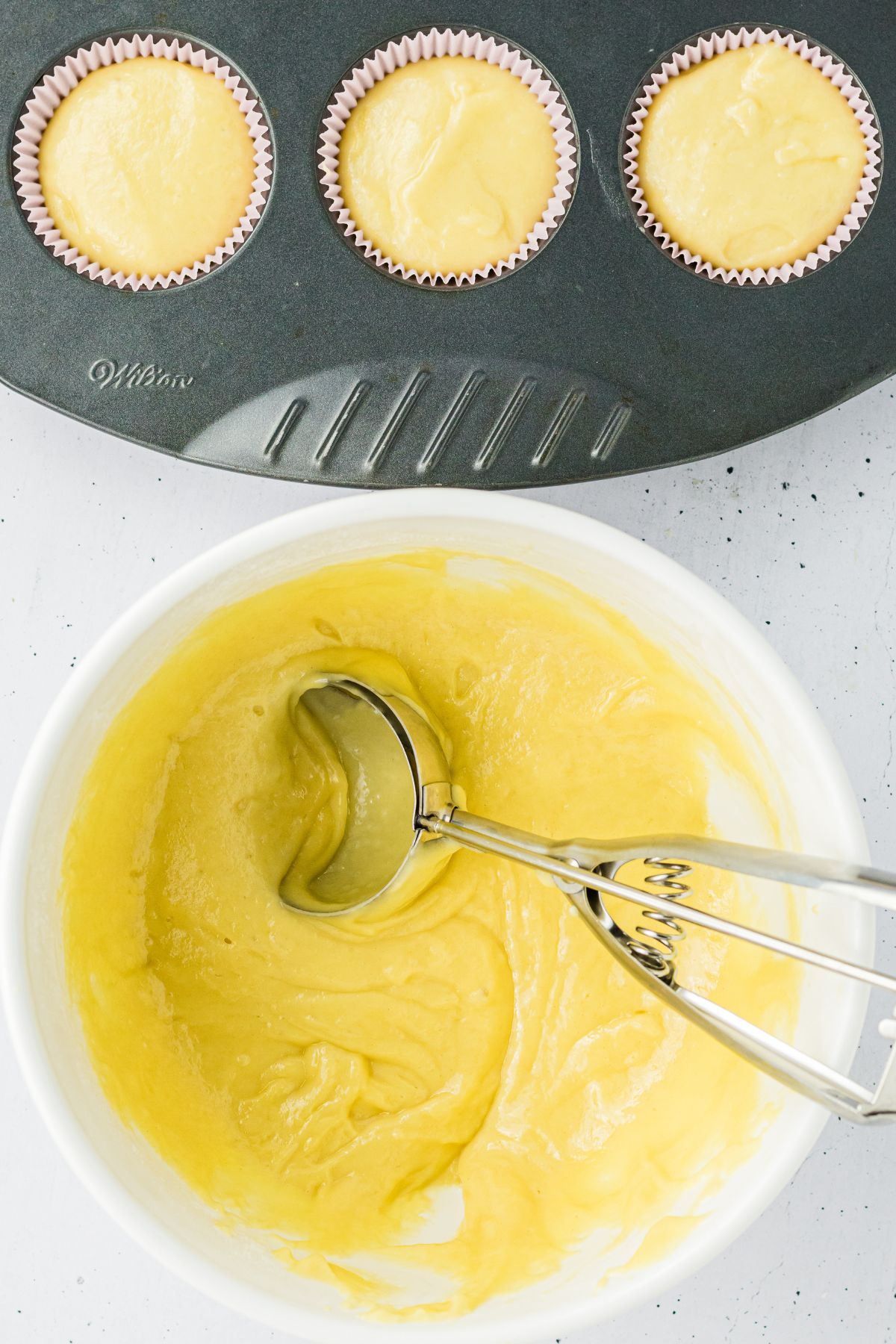 Cake batter being scooped into paper liners to make cupcakes. 