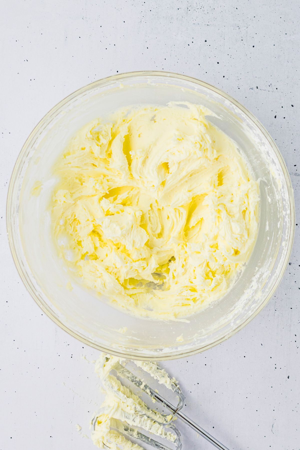 Buttercream frosting being mixed in a clear glass mixing bowl. 