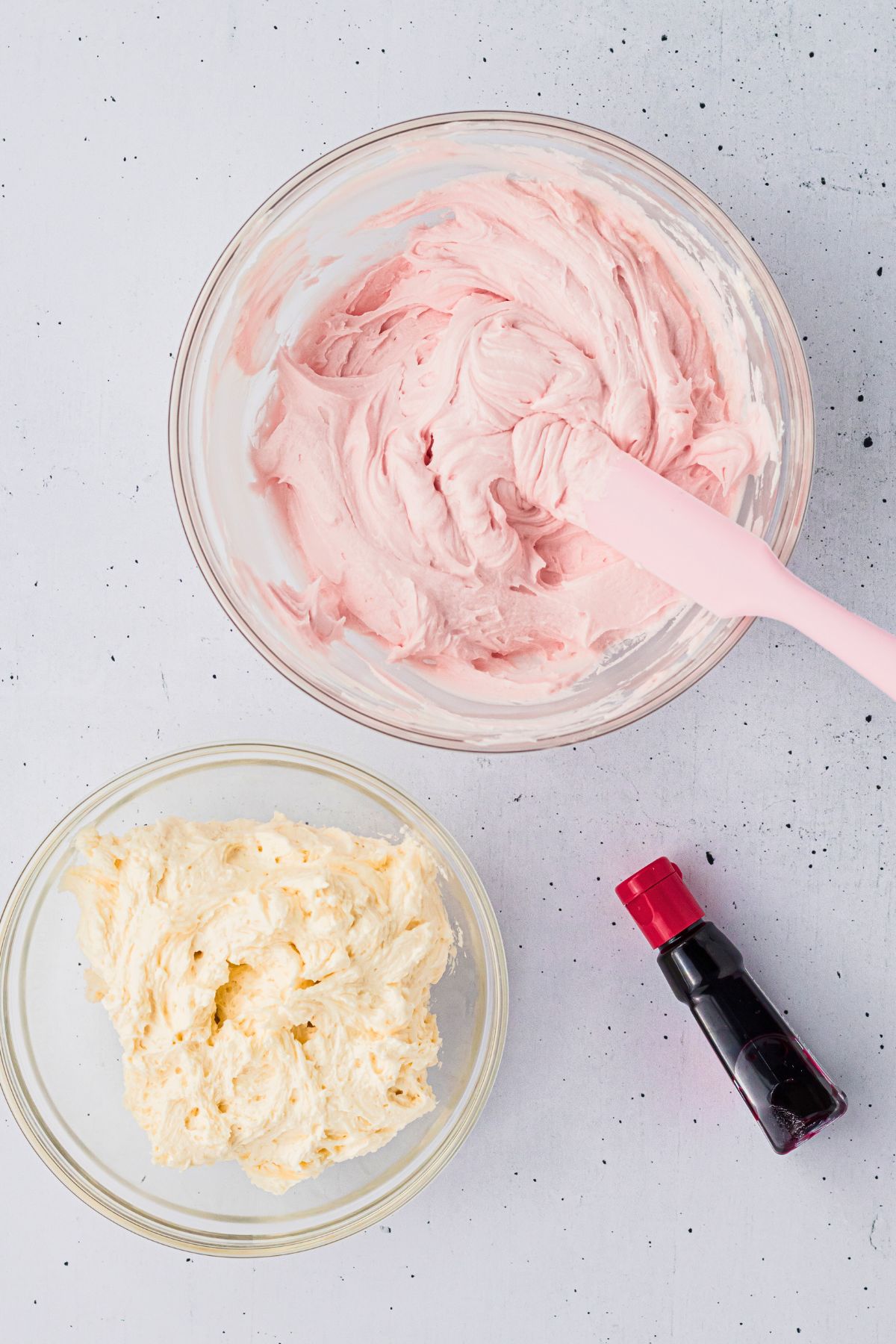 Buttercream frosting divided into two bowls, with one bowl having pink coloring added making pink frosting. 