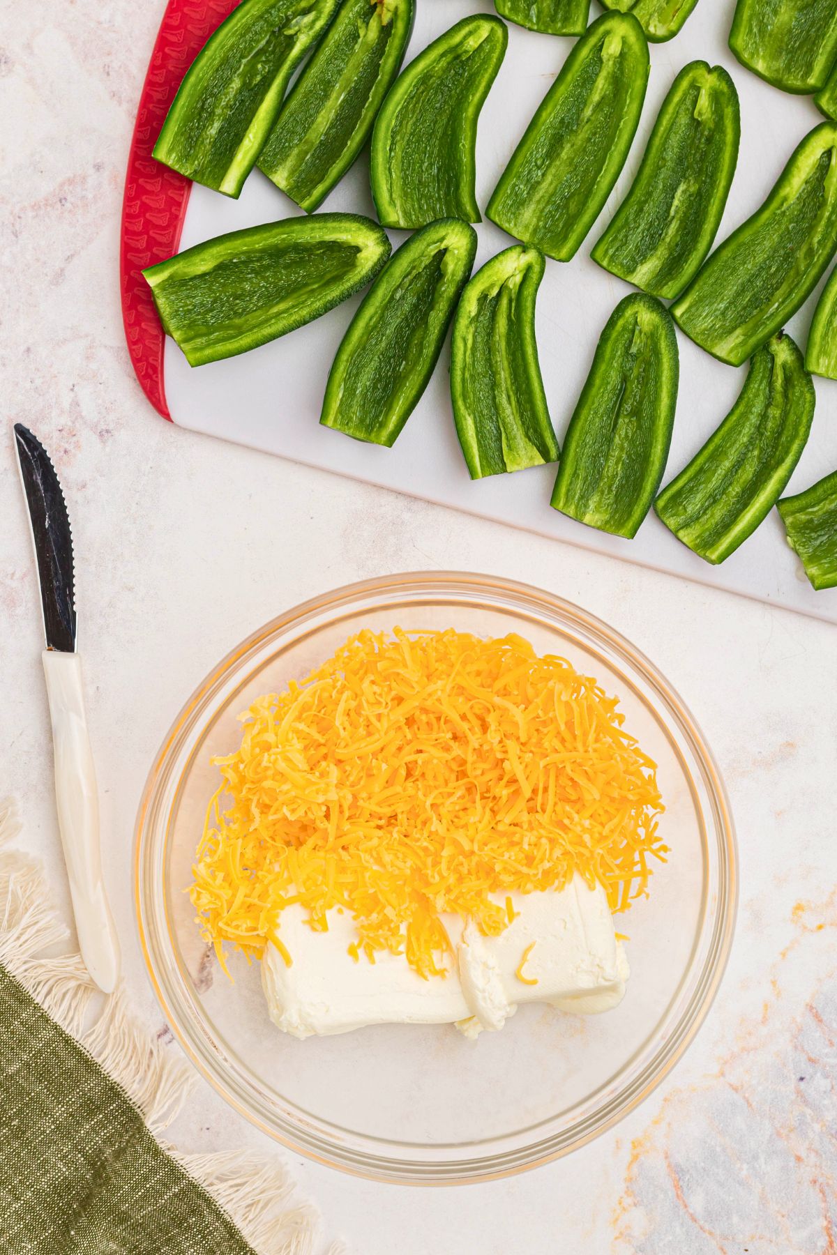 Jalapeno peppers with seeds and membranes removed, and a bowl with cheddar and cream cheese being mixed in a bowl. 