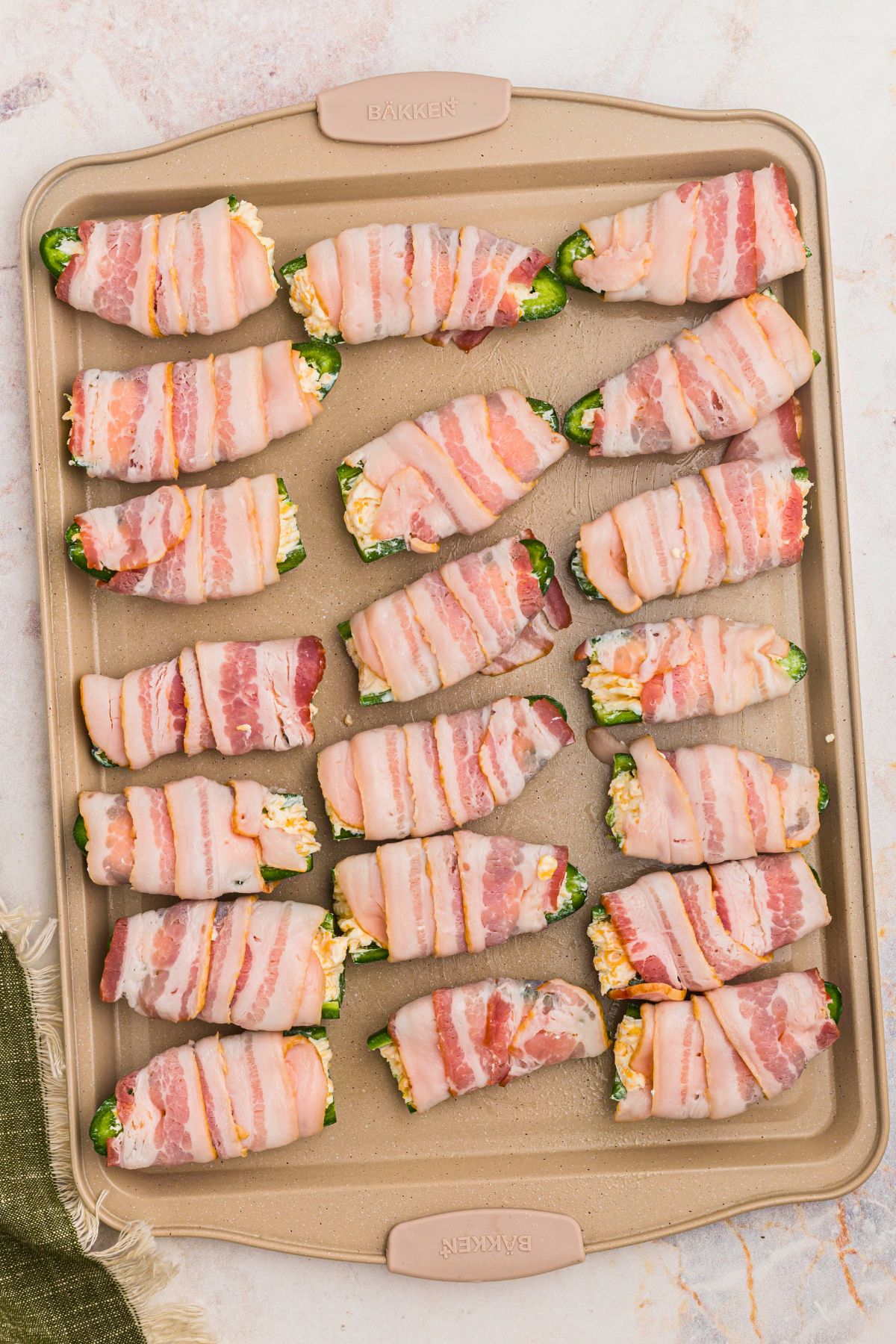 baking sheet with bacon wrapped cheese stuffed jalapenos on top before baking. 