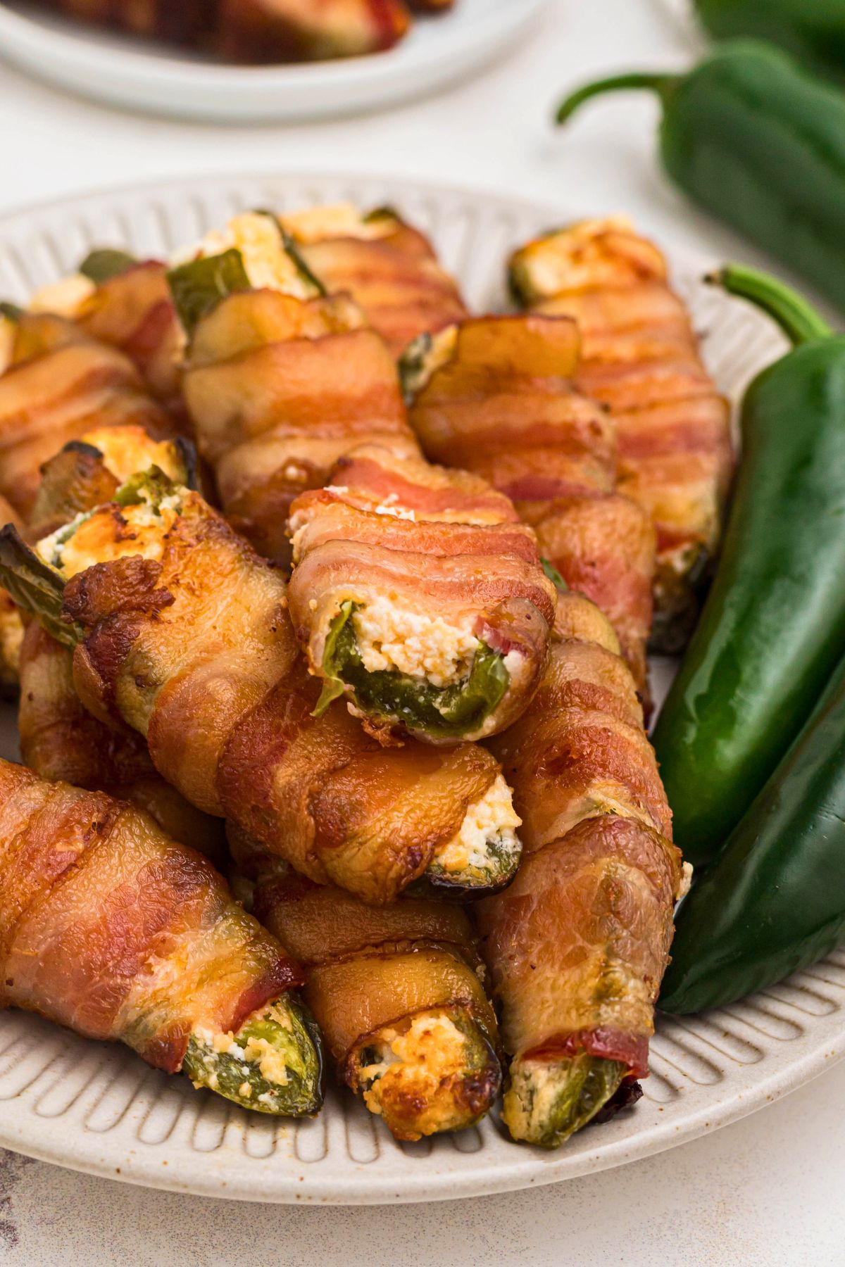 Bacon wrapped jalapeno poppers stacked with one on top having a bite taken. 