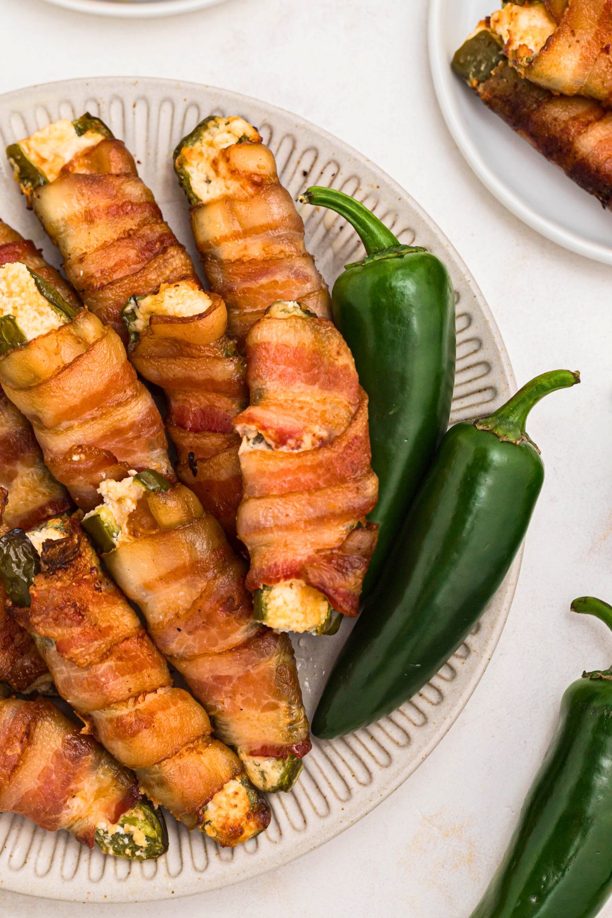 Crispy bacon wrapped jalapenos filled with cheese, stacked on a white plate. 