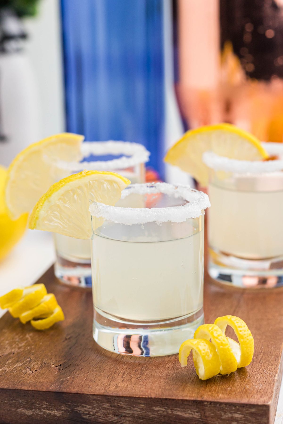 Sugar rimmed shot glass with lemon wedge for garnish, and lemon curls in front of glasses, after being filled with lemon drop shots.