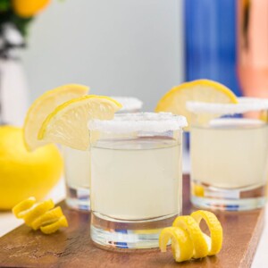 Sugar rimmed shot glass with lemon wedge for garnish, and lemon curls in front of glasses, after being filled with lemon drop shots.