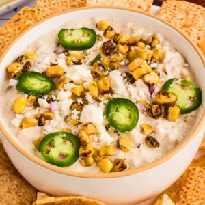 Creamy Mexican corn dip in a white bowl, surrounded by tortilla chips for dipping.