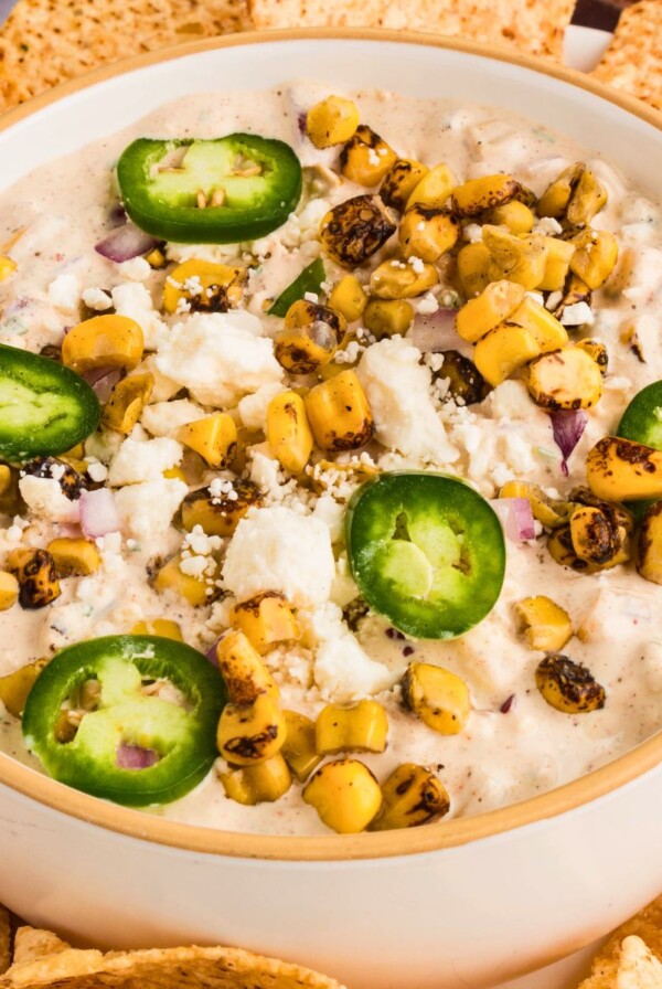 Creamy Mexican corn dip in a white bowl, surrounded by tortilla chips for dipping.