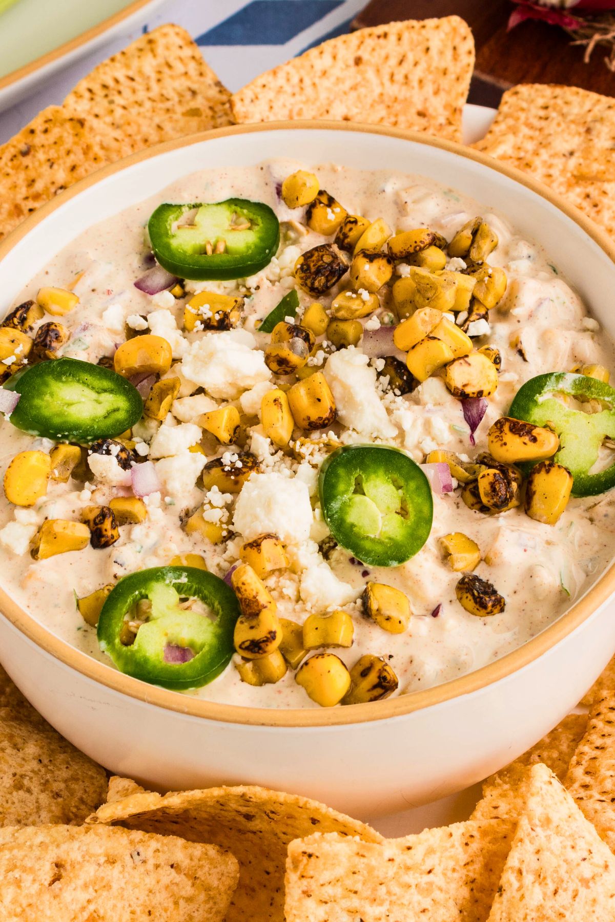 Creamy Mexican street corn dip in a white bowl surrounded by tortilla chips. 