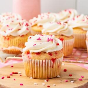 White cupcakes with pink sprinkles baked in the batter, then frosted with white frosting and topped with pink sprinkles.