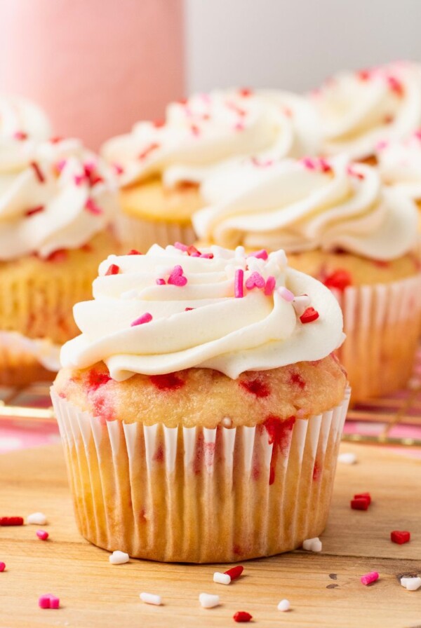 White cupcakes with pink sprinkles baked in the batter, then frosted with white frosting and topped with pink sprinkles.