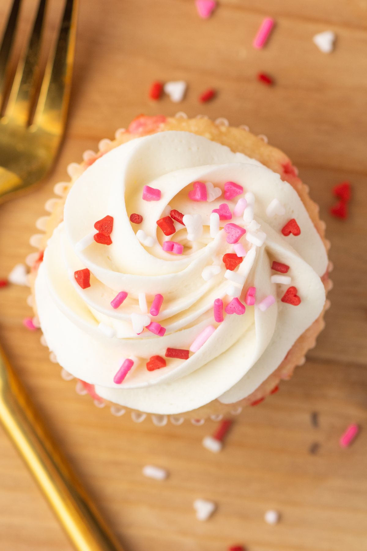 White cupcakes with white frosting and pink sprinkles on a wooden cutting board. 