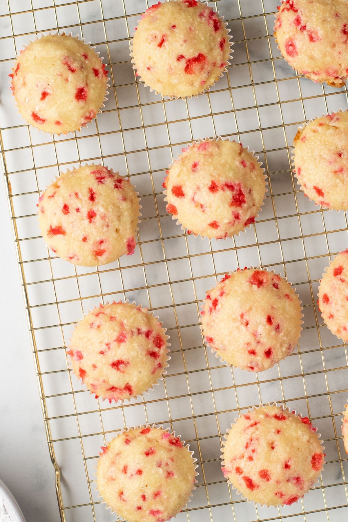 Baked cupcakes with pink sprinkles in them, on a cooking rack. 