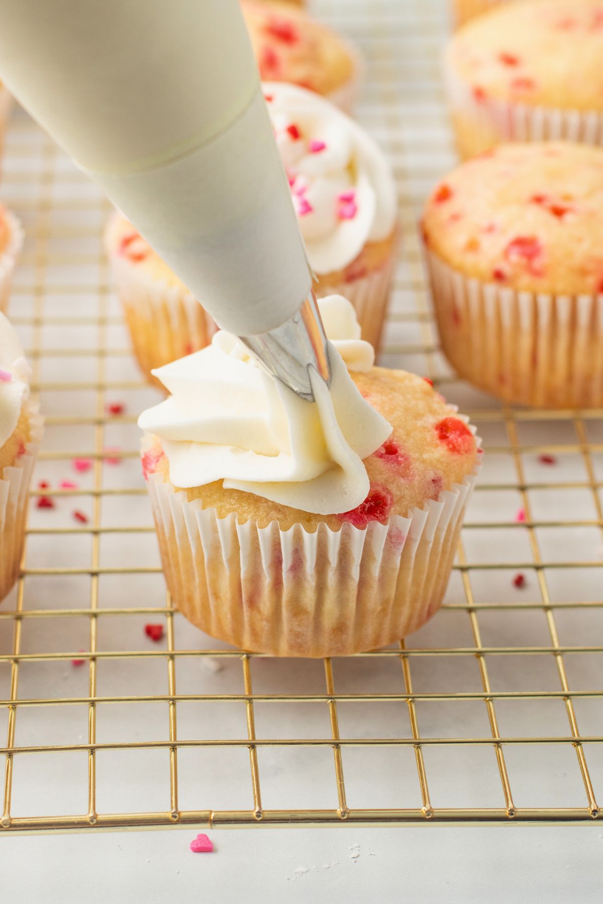 Pink sprinkled cupcake being frosted with buttercream frosting. 