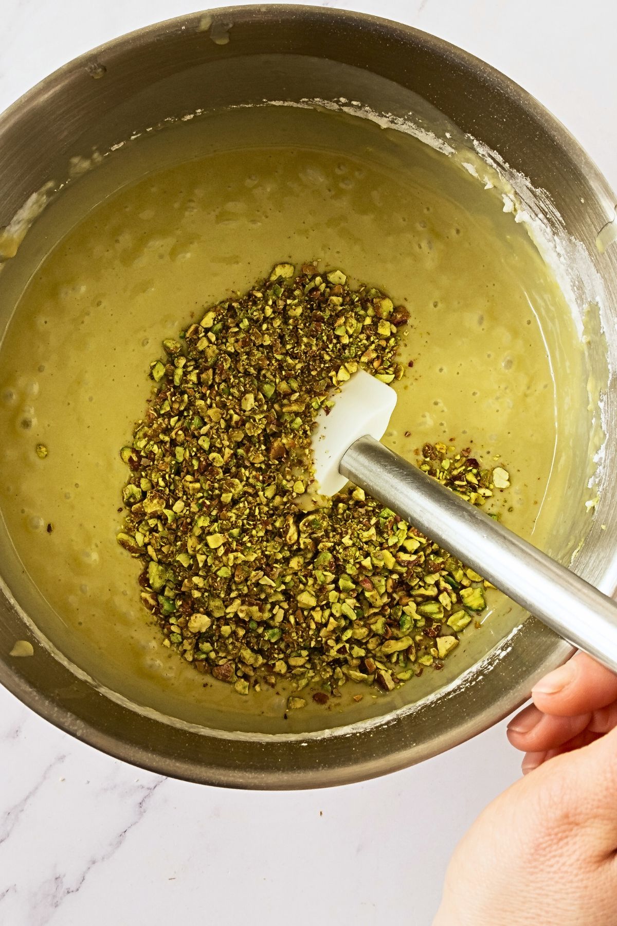 Chopped pistachios being folded into cake mix in a silver bowl. 