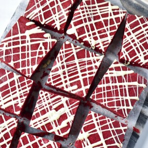 Bright red brownies cut into squares with white chocolate drizzled on top.