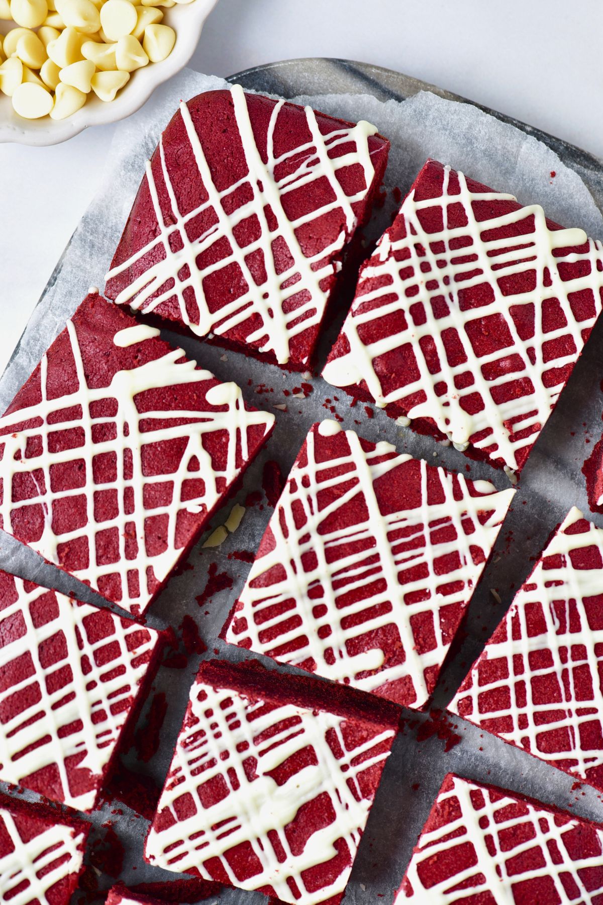 Bright red brownies cut into squares with white chocolate drizzled on top. 